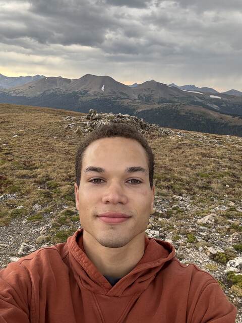 Carlos Eckert on a mountain ridge above the treeline with peaks and clouds behind